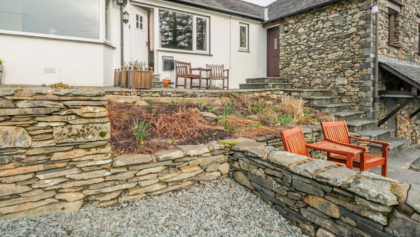 A stone-walled garden with a seating area and a white building with a stone facade. - Kirkstone Cottage (Ambleside)