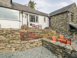 A stone-walled garden with a seating area and a white building with a stone facade. - Kirkstone Cottage (Ambleside)