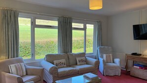 A living room with a beige sofa set, a glass coffee table, and a television mounted on the wall. - Woodlands Cottage (Dorchester)