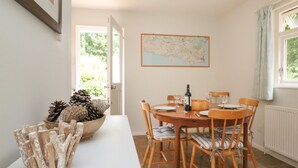 A dining area with a round table, chairs, a bowl of pinecones, a wine bottle, and a map on the wall. - Woodlands Cottage (Dorchester)