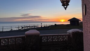 Vista al atardecer desde un paseo marítimo con un farol y una pequeña estructura a lo lejos.
