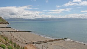 Una playa costera con un paseo marítimo, mar tranquilo y montañas a lo lejos.