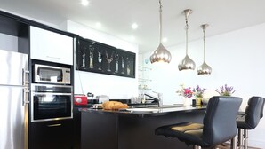 Una cocina moderna con electrodomésticos de acero inoxidable, una isla central con taburetes de bar, iluminación colgante y un elemento decorativo en la pared.