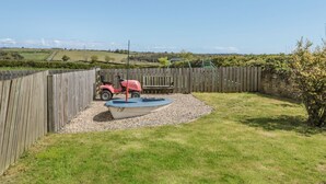 Ein von einer Hecke umgebener Garten mit einem kleinen Boot, einem roten Spielzeugauto und einer Schaukel.