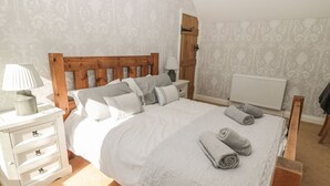 Ein Schlafzimmer mit einem hölzernen Bettgestell, weißer Bettwäsche, einem Nachttisch mit Lampe und einer Heizung.