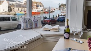 A cozy seating area with a view of a harbor, a bottle of Cava wine, and two glasses on a table. - Harbour Edge (Weymouth)