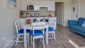 A compact kitchen with white cabinets, a microwave, and a gas stove. There is a dining table with four chairs, and a blue sofa in the living area.