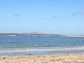 Una playa con aguas tranquilas, orilla arenosa y montañas a lo lejos.