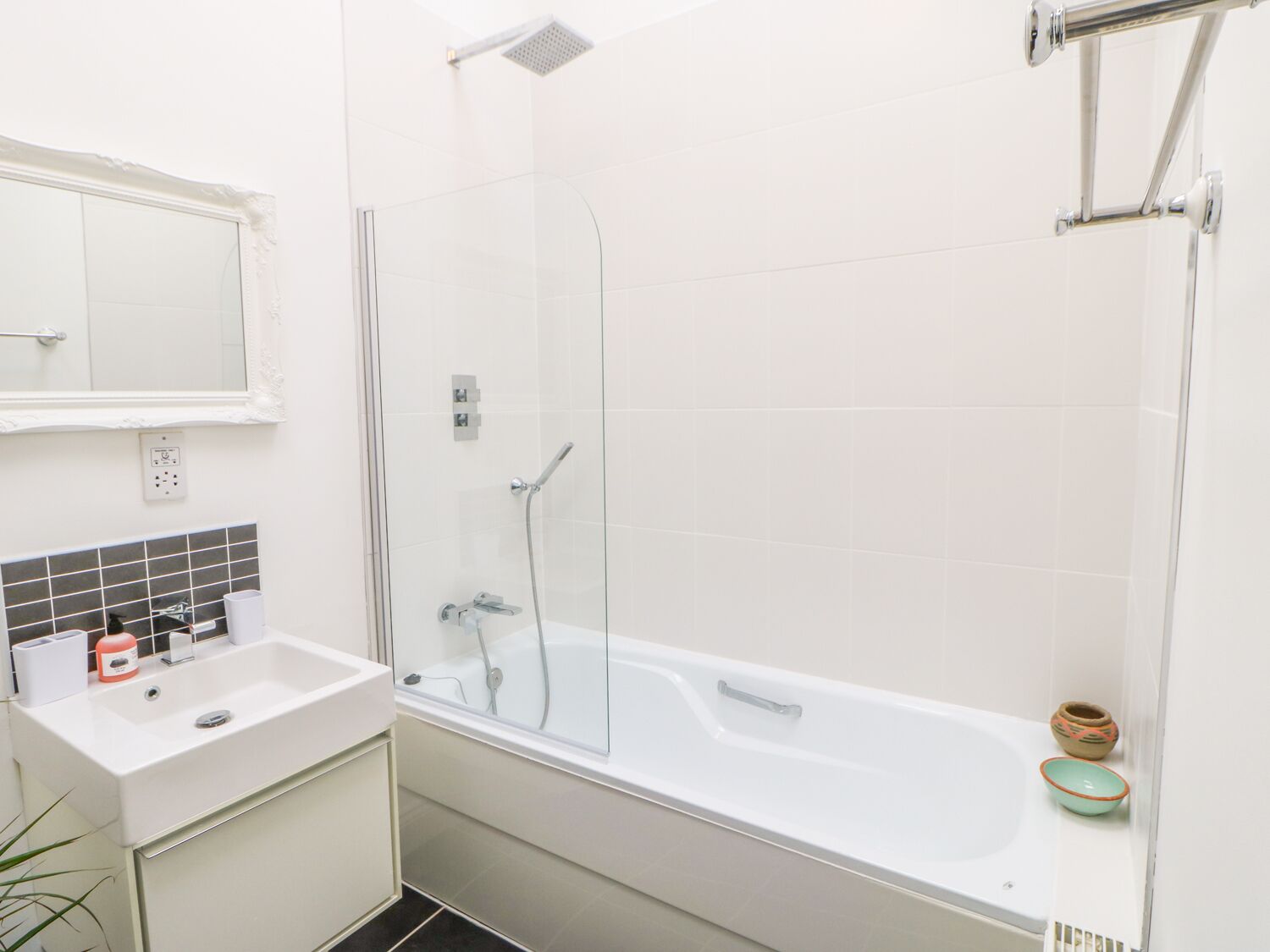 A modern bathroom with a glass-enclosed shower, a white bathtub, and a sink with a mirror above it.