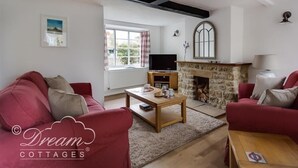 A cozy living room with red sofas, a stone fireplace, a television, and a window with curtains. - Bramble Cottage (Bridport)