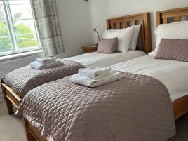 Una cama doble con cabecera de madera, una mesita de noche con lámpara y una ventana con cortinas.