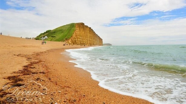 A beach with a large cliff and a sandy shore. - Bramble Cottage (Bridport)