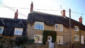 A traditional stone house with a thatched roof, multiple windows, and a stone wall. - Bramble Cottage (Bridport)