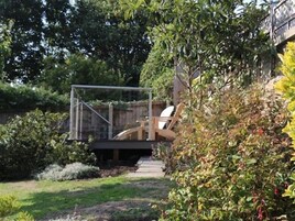 Un jardín con terraza de madera, una silla y un pequeño puente.
