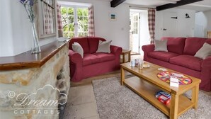 A cozy living room with two red sofas, a wooden coffee table, and a stone fireplace. - Bramble Cottage (Bridport)