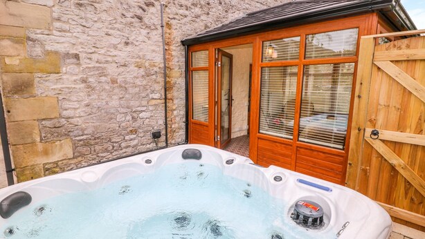 Ein Whirlpool in einem von Steinmauern umgebenen Außenbereich mit einer Holztür und Fensterläden.