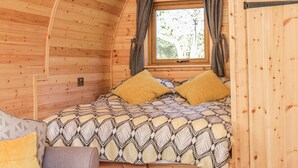 A cozy cabin room with a bed, a sofa, and a window with curtains. - Dingle Den (Hereford)