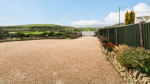 A gravel driveway leading to a white gate, surrounded by a stone wall and red flowers. - Burton Bay (Bridport)