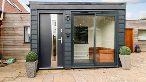 A modern building with a dark exterior, large sliding glass doors, and a stone planter with a spherical plant on the ground. - Burton Bay (Bridport)