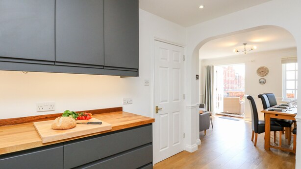 A modern kitchen with dark cabinets, a wooden countertop, and a cutting board with vegetables. - Ashwood (Weymouth)