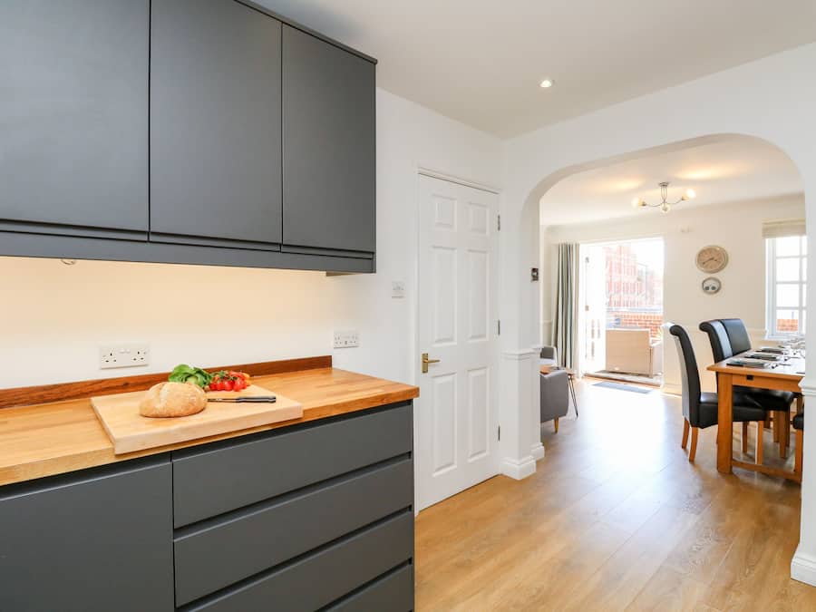 A modern kitchen with dark cabinets, a wooden countertop, and a cutting board with vegetables.