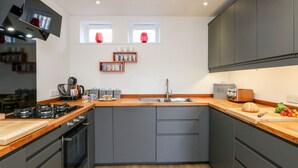 A modern kitchen with grey cabinets, a wooden countertop, a built-in oven, and a window above the sink. - Ashwood (Weymouth)