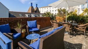 An outdoor patio with wicker furniture, a table with wine glasses, and a large umbrella. - Ashwood (Weymouth)