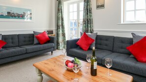 A living room with two grey sofas, red and grey cushions, a wooden coffee table with a fruit bowl and wine glasses, and a bottle of wine. - Ashwood (Weymouth)