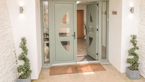 Une entrée moderne avec une porte verte, un petit jardin intérieur et une porte en bois à l’arrière-plan.