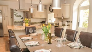 Un espace repas avec une longue table dressée pour six personnes, entourée de fauteuils en cuir foncé.