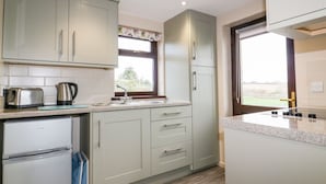 Eine moderne Küche mit hellen Schränken, einem Edelstahlkühlschrank, einem Wasserkocher und einem Fenster mit Blick ins Freie.