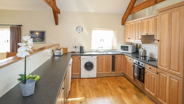 A spacious kitchen with wooden cabinets, a washing machine, a microwave, and a sink.