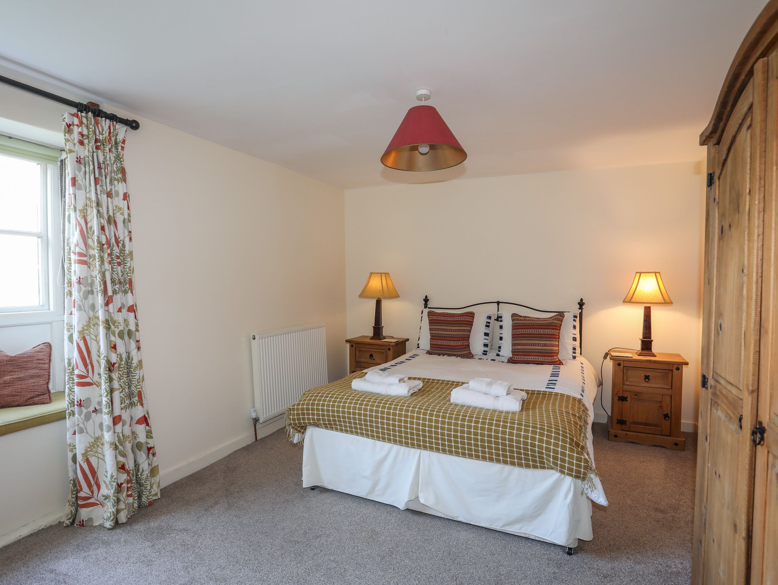 Une chambre à coucher avec un lit, deux tables de chevet avec des lampes, un radiateur et une fenêtre avec des rideaux.