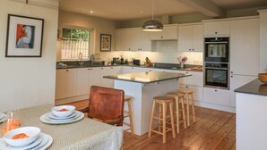 Una cocina moderna con armarios blancos, una isla central, taburetes de madera y una mesa de comedor preparada para el desayuno.