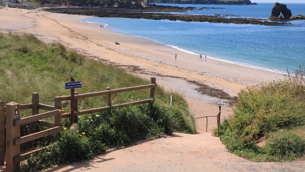 Una playa costera con una valla de madera y un letrero que indica prohibido estacionar.