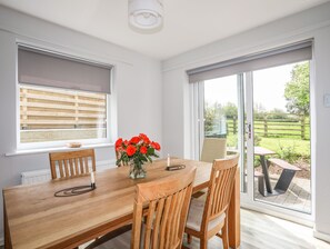 A dining area with a wooden table, chairs, a vase with flowers, and a view of the garden through large windows. - Bronallt (Y Felinheli)