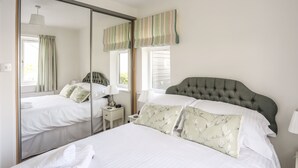A bedroom with a large mirror, a tufted headboard, a bedside table with a lamp, and a window with curtains.