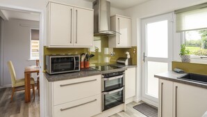 A modern kitchen with white cabinets, a built-in microwave, double ovens, and a window with a view of greenery.