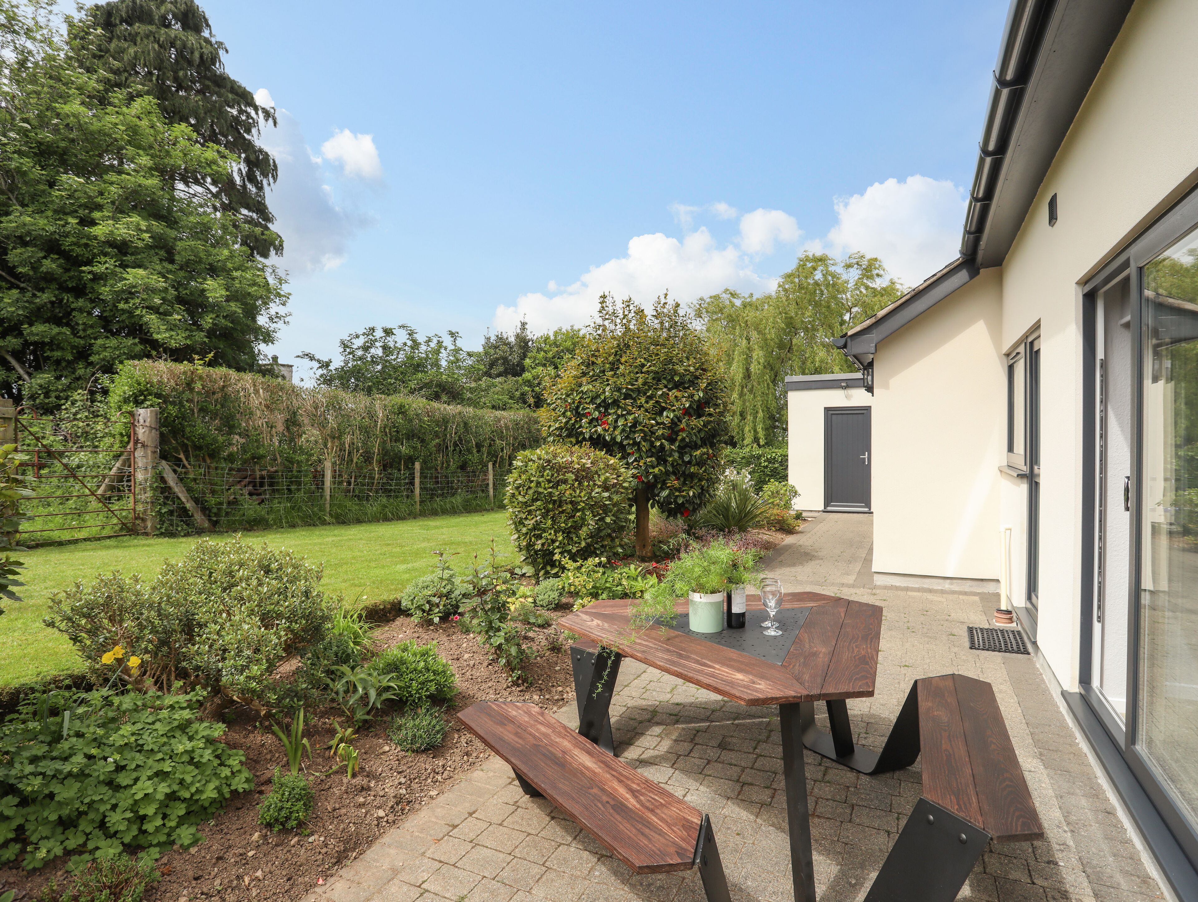 A patio with a table and benches, surrounded by a garden with various plants and a fence.