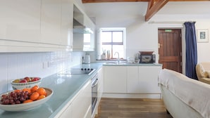 A modern kitchen with white cabinets, a glass countertop, and wooden beams on the ceiling.