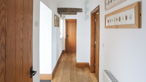 A hallway with wooden flooring, a wooden door on the left, and a framed leaf artwork on the right wall.