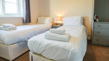 Habitación de hotel con dos camas, cada una con ropa de cama y toallas blancas, una mesita de noche con lámpara y un armario.