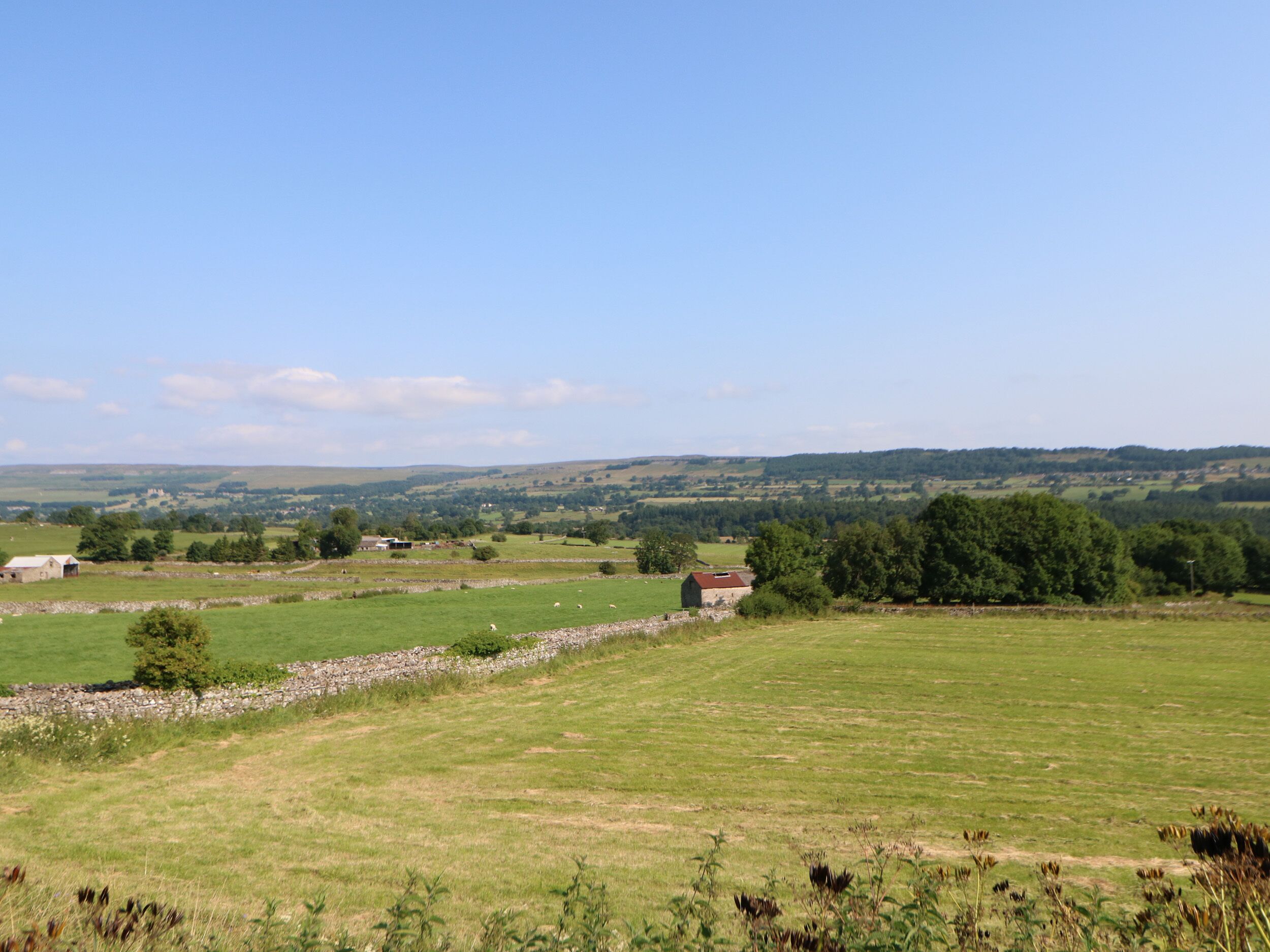 A rural landscape with fields, a stone wall, and a small building.