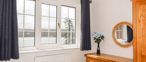 A bedroom with a bed, a wooden dresser, a mirror, and a window with curtains.