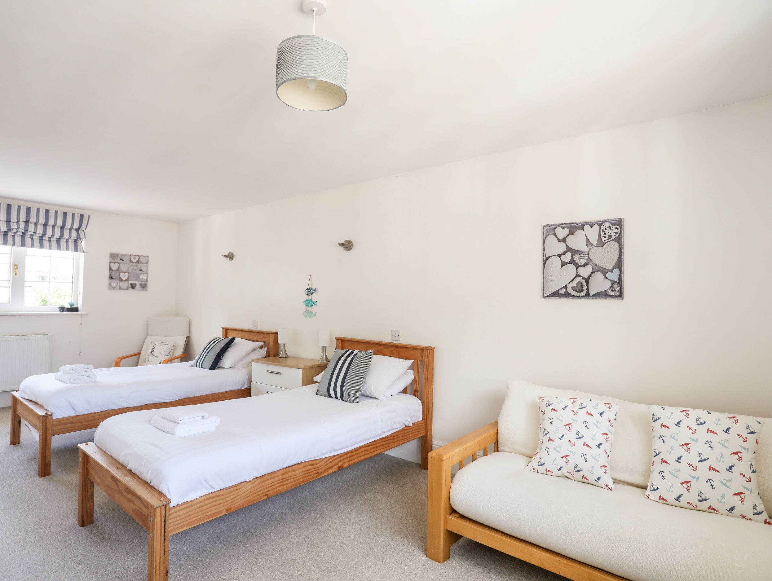 A bedroom with two wooden beds, a sofa, a hanging light fixture, and heart-themed wall art.
