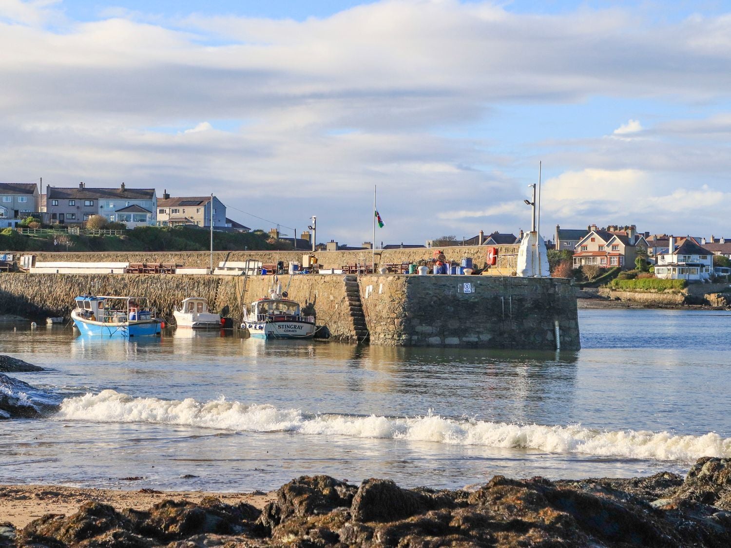 Un puerto costero con barcos amarrados, un muelle de piedra y casas al fondo.