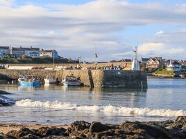 Un puerto costero con barcos amarrados, un muelle de piedra y casas al fondo.