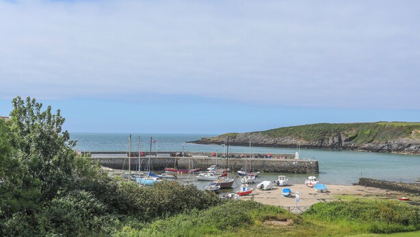 A coastal marina with boats docked, a sandy beach, and a rocky coastline. - Farm Cottage (Cemaes Bay)