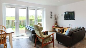 A living room with a sofa, armchair, and a TV mounted on the wall. - Farm Cottage (Cemaes Bay)