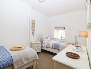 A bedroom with two beds, a bedside table, a lamp, a window, and wall decorations. - Farm Cottage (Cemaes Bay)